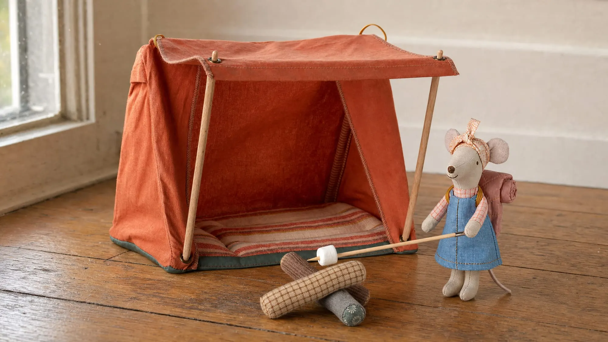 Maileg hiker mouse beside its rust orange tent, pitched on a wood floor, with the bonfire set.
